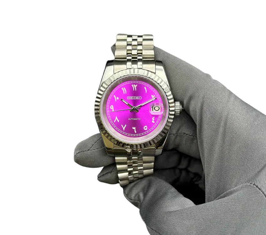 Montre automatique Seiko avec un cadran violet vif, chiffres arabes, bracelet en acier inoxydable, tenue par une main gantée grise.