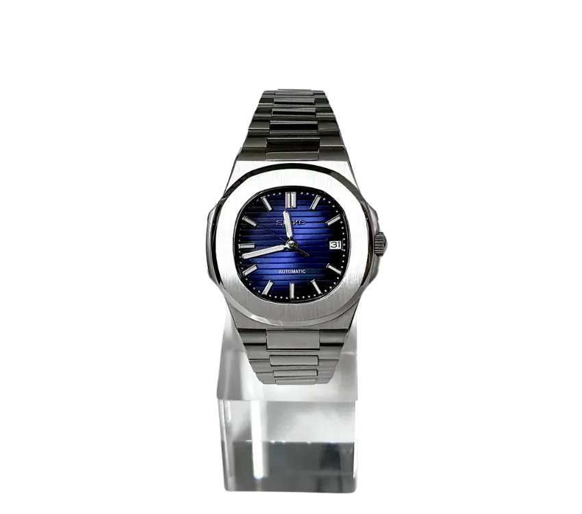 L'image montre une montre automatique Seiko avec un boîtier en acier inoxydable et un cadran bleu à motif horizontal. Les index et les aiguilles sont argentés, et une fenêtre de date est visible à 3 heures. La montre est présentée sur un support transparent, mettant en valeur son design raffiné et son élégance moderne.