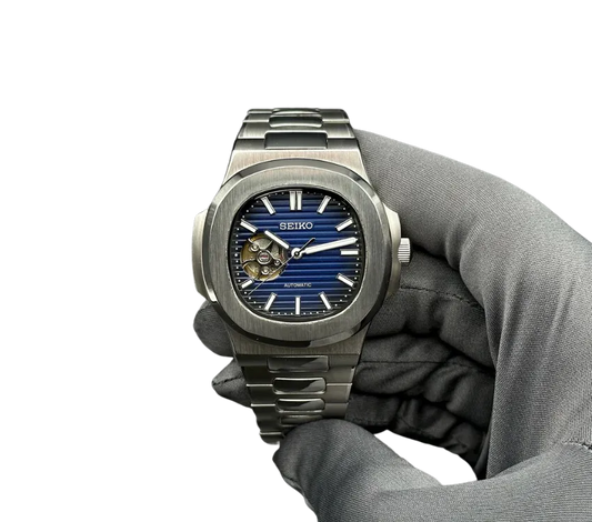 L'image montre une montre Seiko automatique avec un cadran bleu texturé, visible à travers une ouverture révélant son mécanisme interne. La montre est en acier inoxydable, avec un bracelet assorti, et est tenue par une main gantée pour présenter son design élégant.