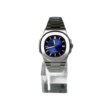 L'image montre une montre automatique Seiko avec un boîtier en acier inoxydable et un cadran bleu à motif horizontal. Les index et les aiguilles sont argentés, et une fenêtre de date est visible à 3 heures. La montre est présentée sur un support transparent, mettant en valeur son design raffiné et son élégance moderne.