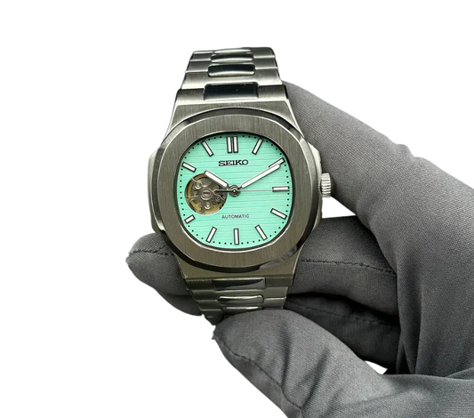 Montre automatique Seiko avec cadran turquoise et ouverture squelettée, bracelet en acier inoxydable, tenue par une main gantée.