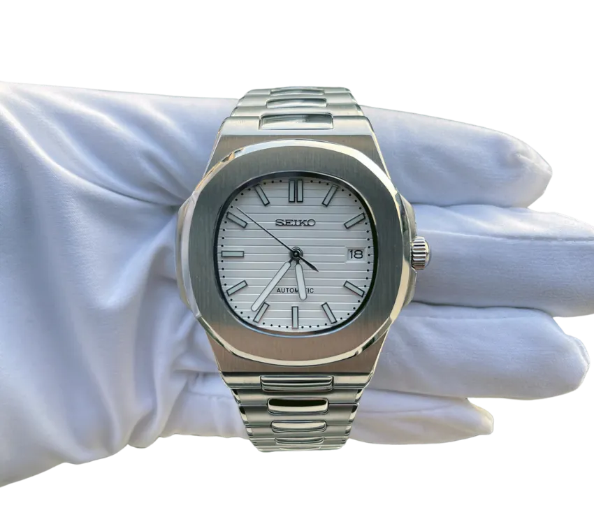 Montre automatique Seiko avec cadran blanc texturé, index et aiguilles argentés, affichage de la date, boîtier en acier inoxydable et bracelet assorti, tenue dans une main gantée blanche.
