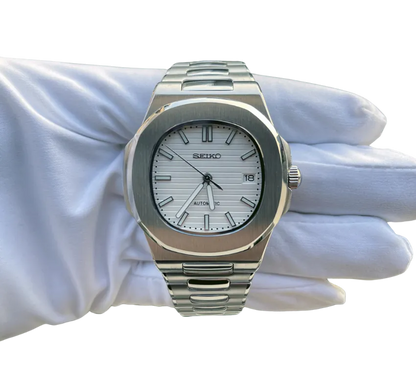 Montre automatique Seiko avec cadran blanc texturé, index et aiguilles argentés, affichage de la date, boîtier en acier inoxydable et bracelet assorti, tenue dans une main gantée blanche.