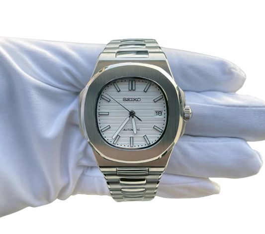 Montre automatique Seiko avec cadran blanc texturé, index et aiguilles argentés, affichage de la date, boîtier en acier inoxydable et bracelet assorti, tenue dans une main gantée blanche.